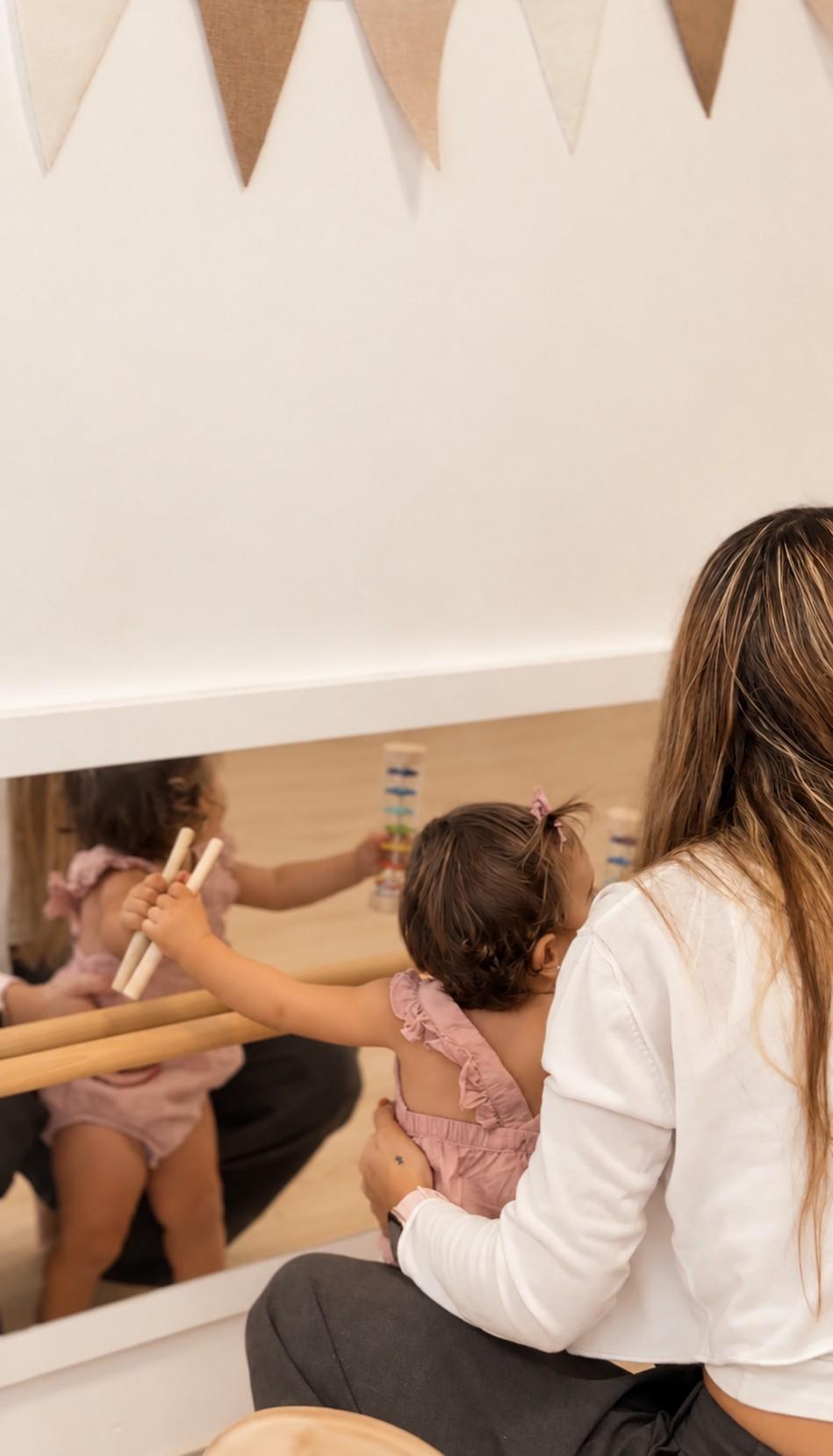 Una educadora y una bebé juegan juntas frente al espejo